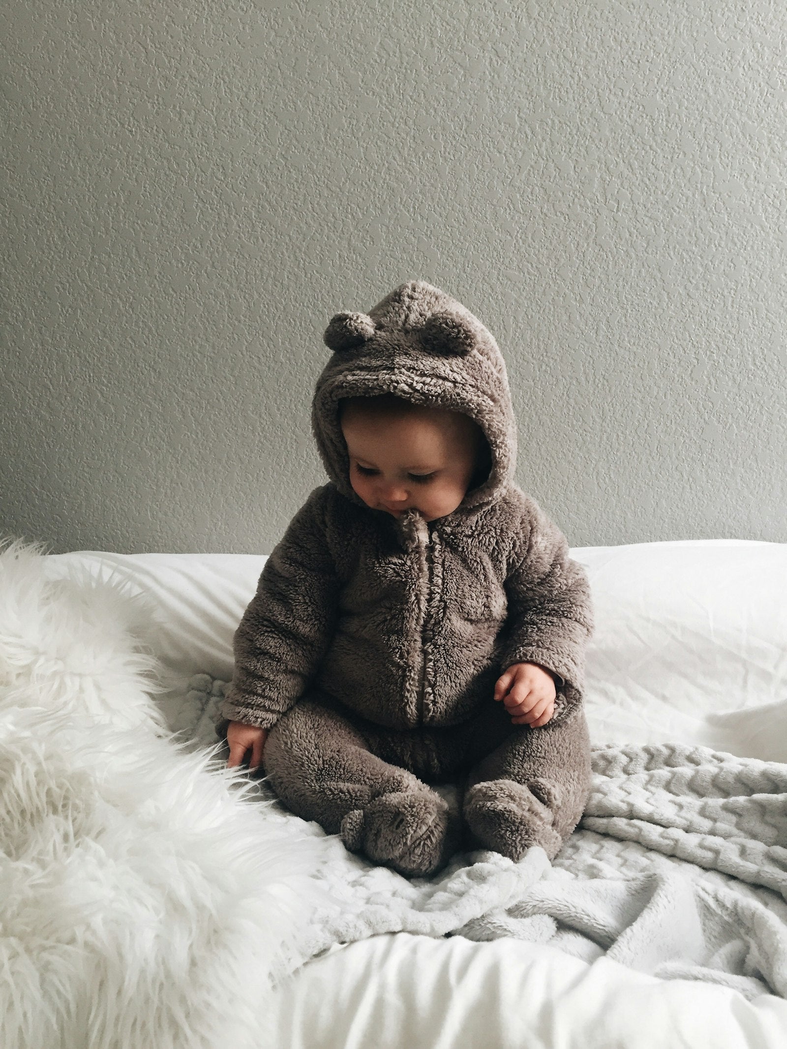 Baby in a cosy bear romper sitting on a soft white bed